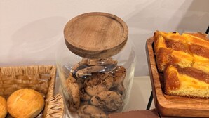 A table with a glass jar of cookies, a basket of bread rolls, and a tray of chocolate bars. - Mostay Boutique Hotel (Mostar)