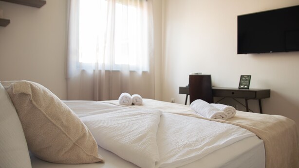 A hotel room with a bed, pillows, a desk, a chair, and a flat-screen TV mounted on the wall. - Mostay Boutique Hotel (Mostar)