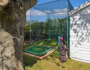 Un espace d’entraînement au golf doté d’un enclos protégé par un filet, d’un green d’entraînement et d’un sac de golf.