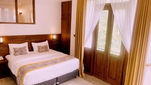 A hotel room with a large bed, wooden headboard, a nightstand, a mirror, and a door with curtains. - Ceylon Ayu Resort - Kandy (Kandy)