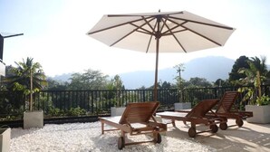 A rooftop terrace with white pebbles, two wooden lounge chairs, a large umbrella, and a view of mountains. - Ceylon Ayu Resort - Kandy (Kandy)