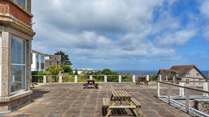 A rooftop terrace with stone flooring, picnic tables, and a view of the sea. - Lovely apartment for 4 guests with WIFI (St Ives)