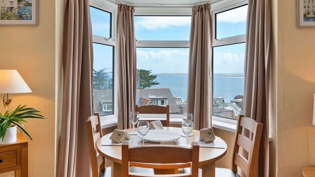 A corner dining area with a table set for two, a potted plant, and a view of the sea. - Lovely apartment for 4 guests with WIFI (St Ives)