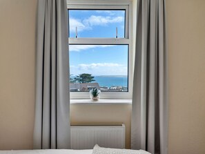 Ein Zimmer mit Fensterblick auf ein Gewässer und einen Baum, einem Heizkörper unter dem Fenster und einem Bett mit weißer Bettdecke.