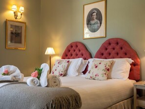 A neatly made bed with floral pillows, a framed portrait on the wall, and a lamp on the side.