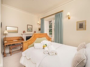 A hotel room with a bed, a desk, a chair, a fireplace, and a window with curtains.