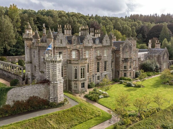 Un château historique en pierre, doté de plusieurs tours, d’un drapeau et d’un jardin bien entretenu.