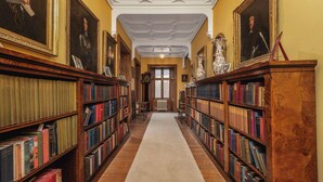 Une bibliothèque avec des étagères de part et d’autre, une allée centrale recouverte de moquette et un plafond orné de moulures décoratives.