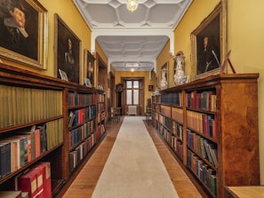 Une bibliothèque avec des étagères de part et d’autre, une allée centrale recouverte de moquette et un plafond orné de moulures décoratives.