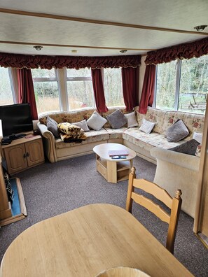 A cozy living area with a sofa, a television, a coffee table, and a dining table. - Caravan in the Trossachs national park (Brig o'Turk)