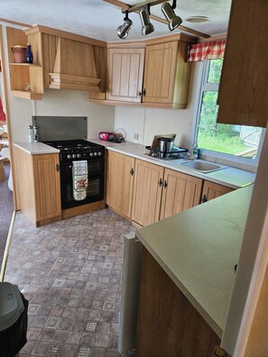 A compact kitchen with wooden cabinets, a gas stove, a sink, and a window with a view of greenery.