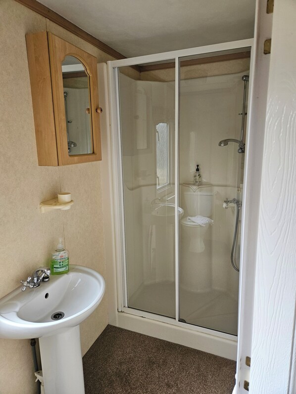 A bathroom with a white sink, a wooden medicine cabinet, a glass-enclosed shower, and a beige tiled floor.