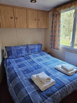 A bedroom with a blue checkered bedspread, wooden headboard, and a window with patterned curtains.