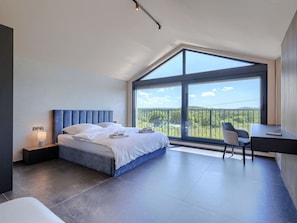 Ein modernes Schlafzimmer mit einem großen Bett, einem Schreibtisch und einem Balkon mit Blick.