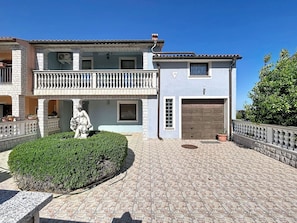 Ein zweistöckiges Gebäude mit Balkon, Garage und einer Statue im Vorgarten.