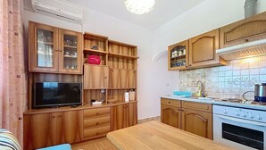 Een compacte keuken met houten kastjes, een inbouwoven en een eethoek met een tafel en bank.