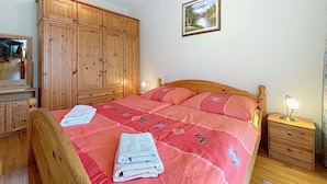 Ein Schlafzimmer mit Bett, Holzschrank, Nachttisch und einem gerahmten Bild an der Wand.