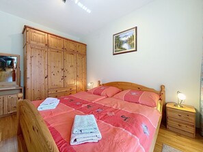 Ein Schlafzimmer mit Bett, Holzschrank, Nachttisch und einem gerahmten Bild an der Wand.