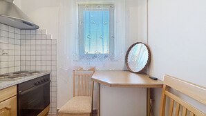 A compact kitchen with a stove, a window with lace curtains, a wooden chair, and a mirror on a table. - Cosy apartment for 2 guests with A/C, WIFI and TV (Banjole)