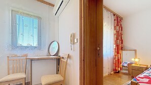 A room with a desk, two chairs, a bed with a lamp, a mirror, a window with a lace curtain, and an air conditioning unit. - Cosy apartment for 2 guests with A/C, WIFI and TV (Banjole)