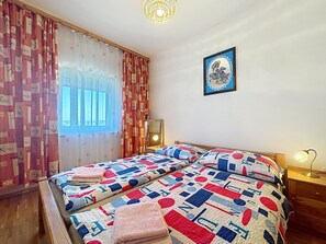 Ein Schlafzimmer mit zwei Betten, einem Vorhangfenster, einem Wandbild und einer Nachttischlampe.