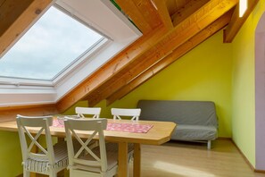 Ein Zimmer mit schrägem Dach, einem Oberlicht, einem Tisch mit Stühlen und einer Couch.