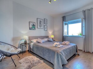 Ein Schlafzimmer mit einem Bett, zwei Nachttischlampen, einem Sessel, einem Teppich und gerahmten Bildern an der Wand.