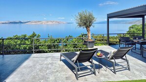 Una terrazza con due poltrone, un tavolo con una ciotola di frutta e un olivo in vaso.