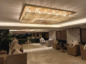 Un hall d’entrée spacieux, agrémenté d’un grand lustre, de fauteuils confortables et d’un escalier en arrière-plan.