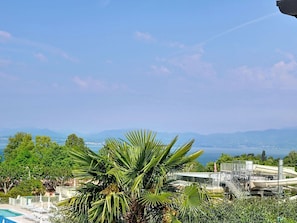 Ein Poolbereich mit Palmen, einer Wasserrutsche und Blick auf das Meer und die Berge.