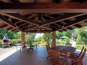 An outdoor patio with a round wooden table and chairs, a grill, and a pizza oven. - Wonderful  villa for 5 guests with WIFI, private pool, patio, pets allowed and panoramic view (Asti)