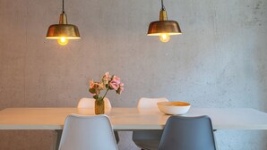 Una mesa de comedor con dos sillas, un jarrón con flores y dos lámparas colgantes.