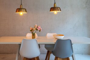Una mesa de comedor con dos sillas, un jarrón con flores y dos lámparas colgantes.