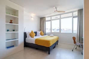 Une chambre dâhĂŽtel moderne, Ă©quipĂ©e dâun lit, dâĂ©tagĂšres intĂ©grĂ©es, dâun bureau et dâune grande fenĂȘtre.