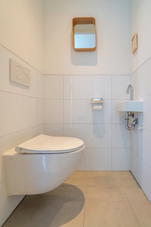 A modern bathroom with a white toilet, a wall-mounted sink, and a mirror.