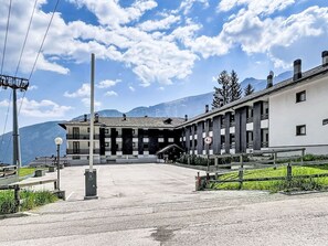 Ein Gebäude im traditionellen Baustil, ein gepflasterter Eingang und eine Bergkulisse im Hintergrund.