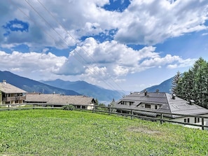 Ländliche Landschaft mit Häusern, einem Feld und Bergen im Hintergrund.