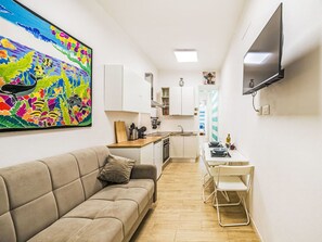 Eine moderne Küche mit weißen Schränken, ein Essbereich mit Tisch und Stühlen, ein beiges Sofa und ein farbenfrohes Bild an der Wand.