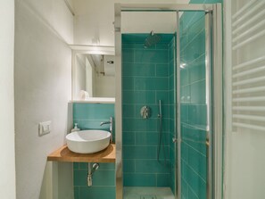 Ein Badezimmer mit einem weißen Waschbecken, einem Spiegel und einer Dusche mit türkisfarbenen Fliesen.