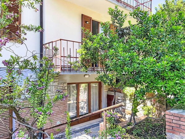 A multi-story building with balconies, a stone facade, and a garden area with various plants. - Beautiful apartment for 3 guests with WIFI, A/C, TV and patio (Rosignano Marittimo)