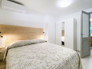 Ein Schlafzimmer mit einem hölzernen Kopfende, einer gemusterten Bettdecke, einer Nachttischlampe und einem Kleiderschrank.