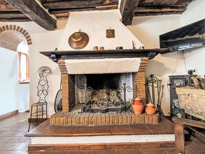 Ein traditioneller Kamin mit Ziegelverkleidung, einem hölzernen Sims und verschiedenen Töpfen und Pfannen darüber.