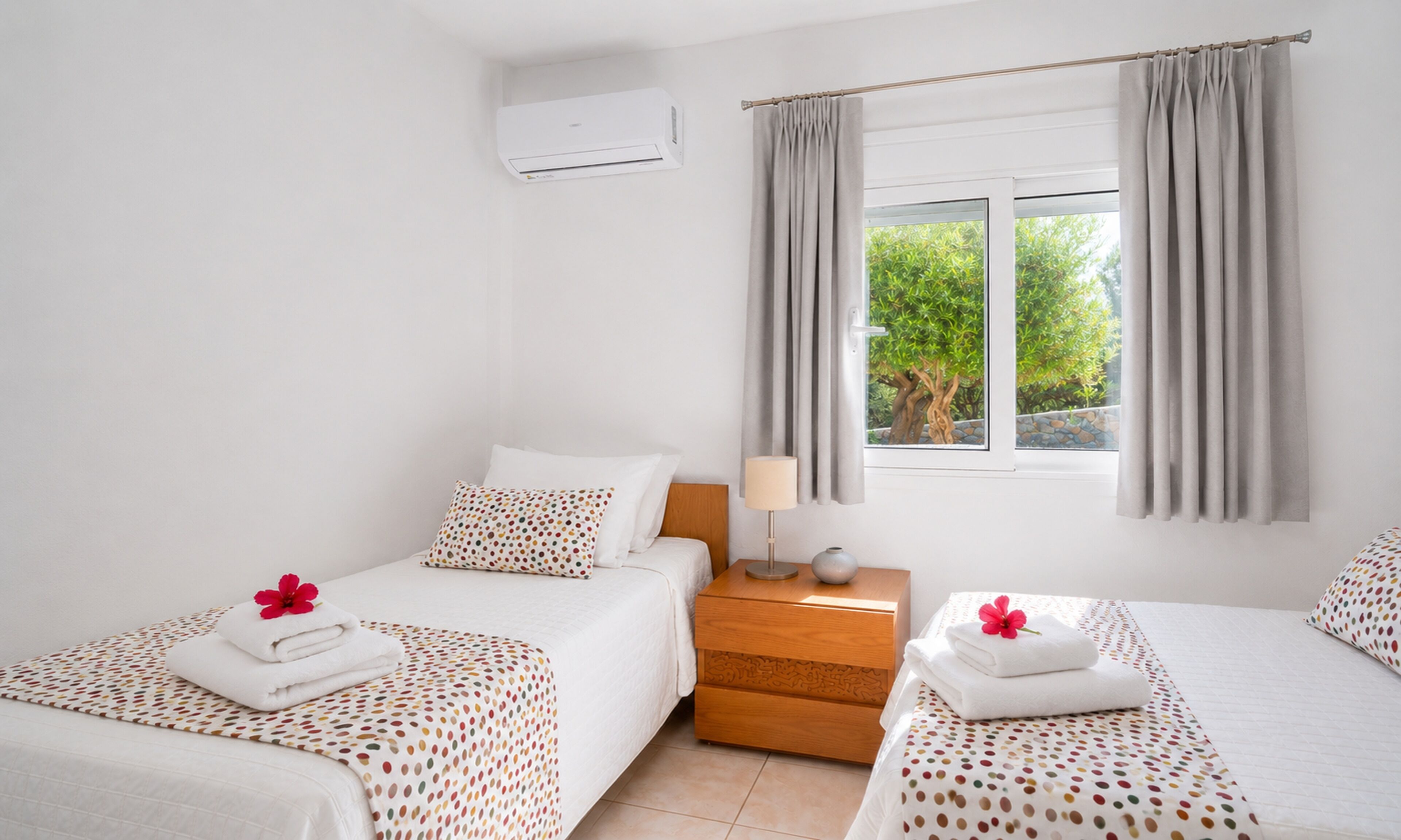 Ein Hotelzimmer mit zwei Betten, einem Fenster mit Vorhängen, einem Nachttisch und einer Klimaanlage.