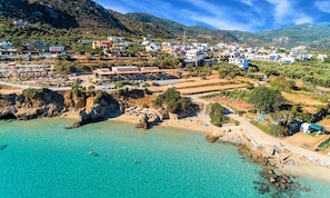 A coastal town with buildings, a beach, and clear turquoise waters. - Olive Green Villa Heated Pool (Agios Nokolaos)