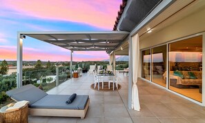 A modern outdoor balcony with a dining area, lounge seating, and a view of the landscape. - Olive Green Villa Heated Pool (Agios Nokolaos)