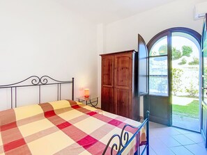 Ein Schlafzimmer mit Bett, Nachttisch, einem Holzschrank und einer Tür zu einem Außenbereich.