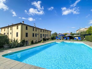 Ein Pool mit Liegestühlen, ein Gebäude mit vielen Fenstern und ein klarer, blauer Himmel.