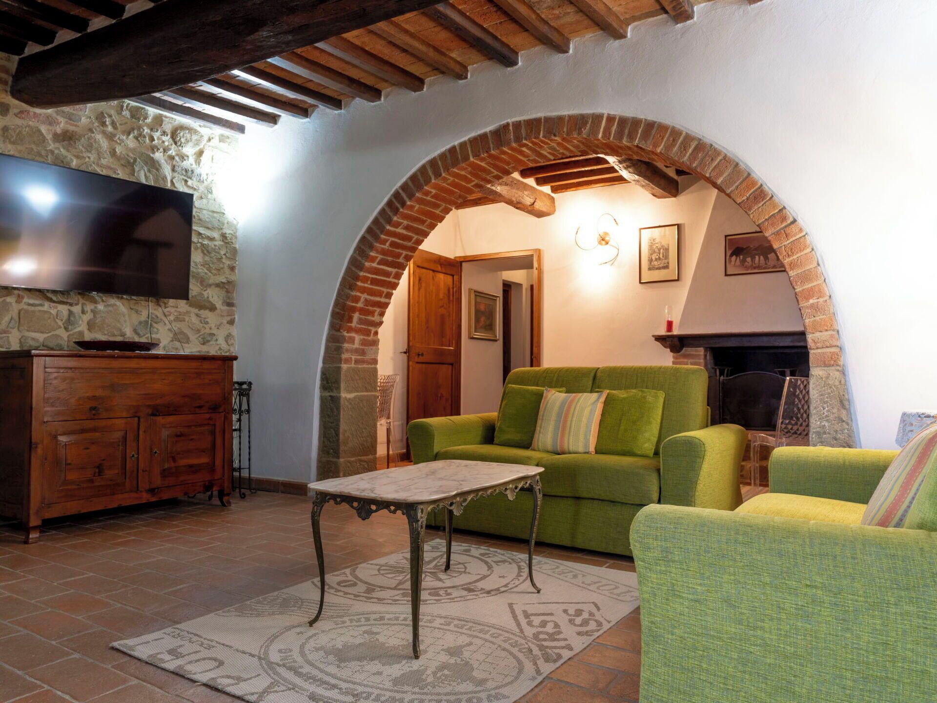 A cozy living room with a green sofa, a wooden cabinet, a TV, and a fireplace.