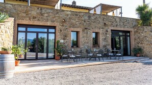 Ein Steinhaus mit großen Fenstern, Außenbestuhlung und einer Schotterterrasse.