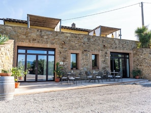 Ein Steinhaus mit großen Fenstern, Außenbestuhlung und einer Schotterterrasse.